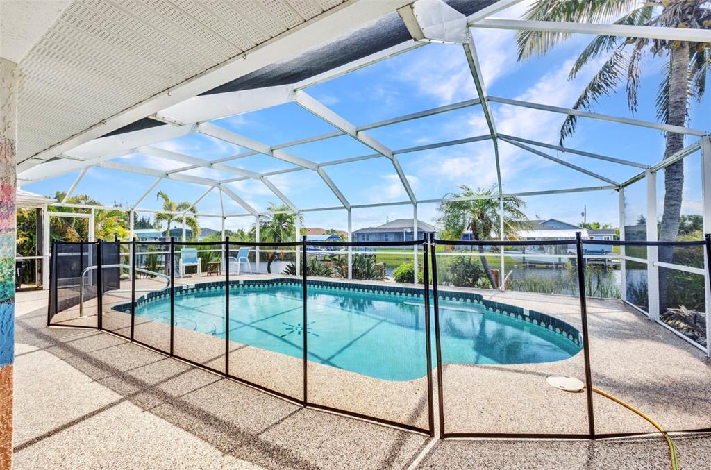 A swimming pool enclosed by a screen cage and a removable safety fence on a patio — 9582 ARSIPE CIRCLE, PORT CHARLOTTE, FL