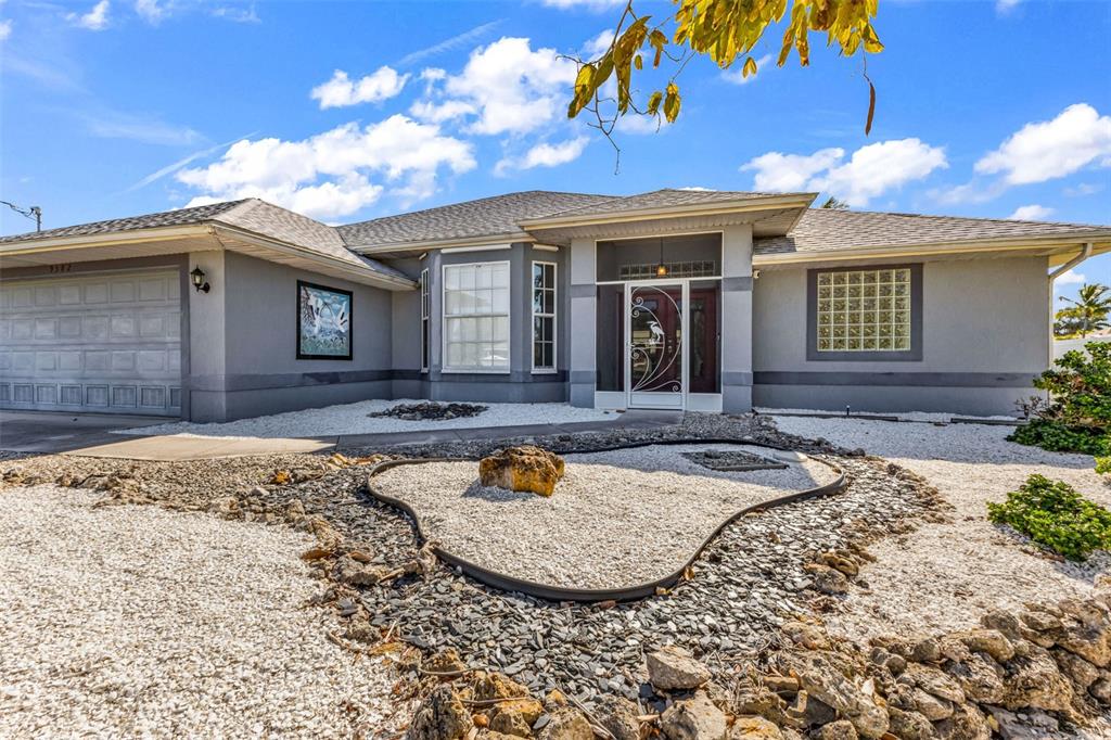 A single-story gray house features a garage, a glass-paneled front door, and rock landscaping — 9582 ARSIPE CIRCLE, PORT CHARLOTTE, FL