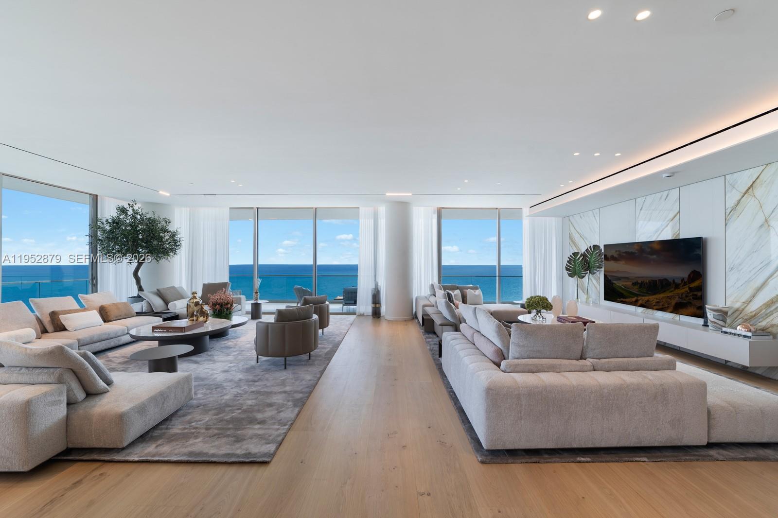 A spacious, modern living room features two large sofas, marble wall paneling, and ocean views — 10203 Collins Ave # 2701, Bal Harbour FL 33154, BAL HARBOUR, FL
