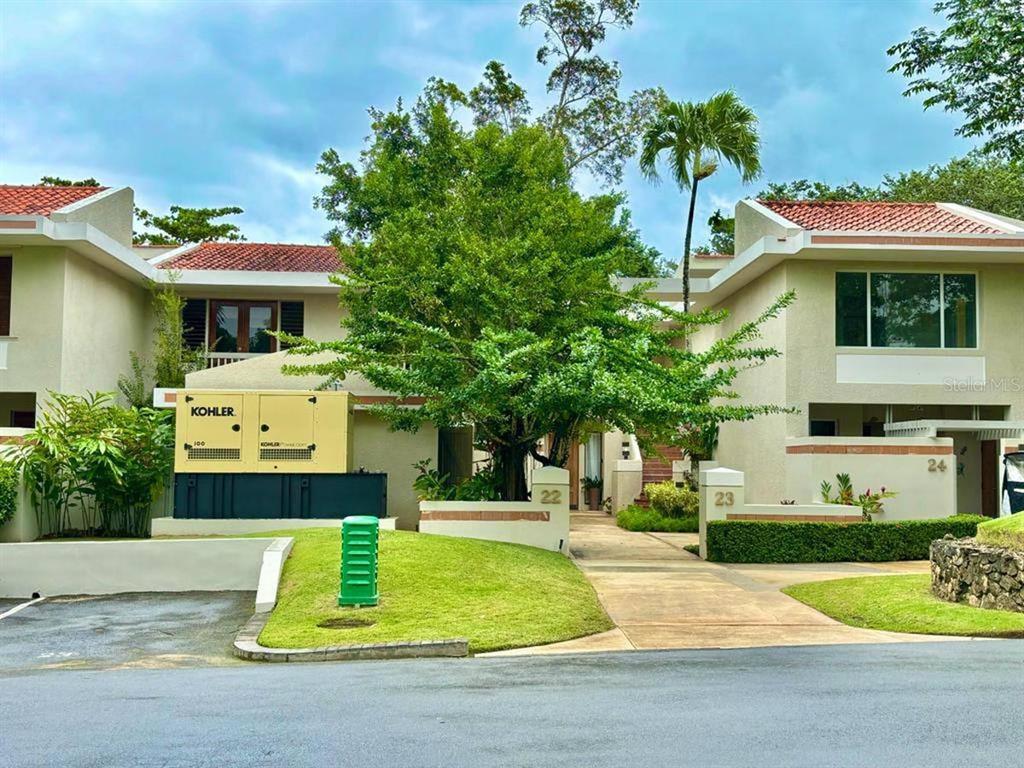A two-story residential building with a Kohler generator, a large tree, and numbered unit entrances — 22 FAIRWAYS VILLAGE DR, DORADO, PR