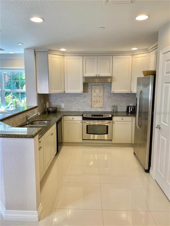 A kitchen features white cabinetry, stainless steel appliances, granite countertops, and light-colored tile flooring — 7652 WHISPER WAY UNIT 104, REUNION, FL