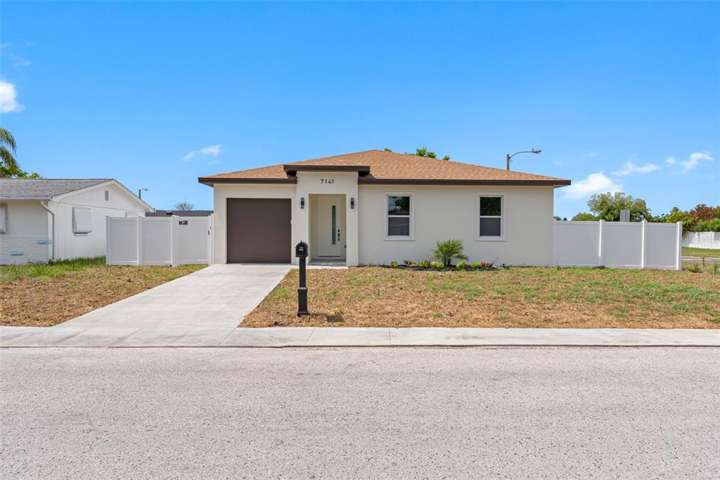 A single-story house with a brown roof, beige stucco exterior, and a concrete driveway — 7141 IVANHOE DRIVE, PORT RICHEY, FL