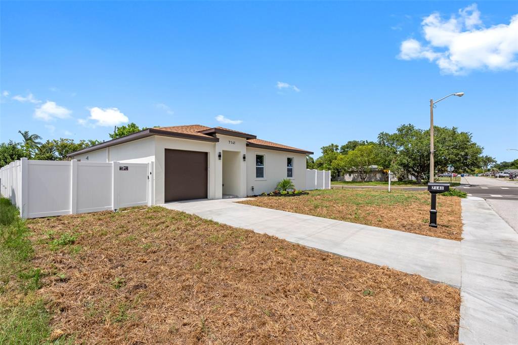 A single-story house with a brown garage door, white vinyl fencing, and a concrete driveway — 7141 IVANHOE DRIVE, PORT RICHEY, FL
