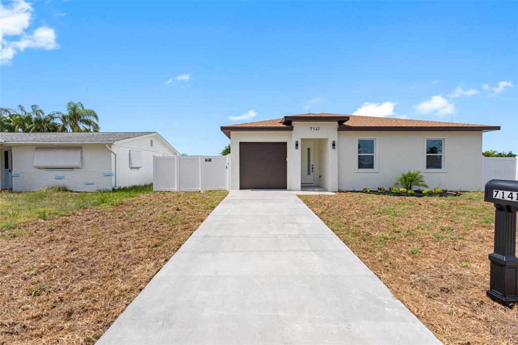 A single-story house with a concrete driveway, brown garage door, and light-colored exterior walls — 7141 IVANHOE DRIVE, PORT RICHEY, FL