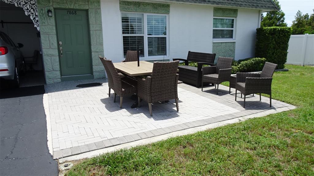 A patio with a dining set and chairs sits outside a house with stone accents — 7868 40TH AVENUE N UNIT 7868, ST PETERSBURG, FL
