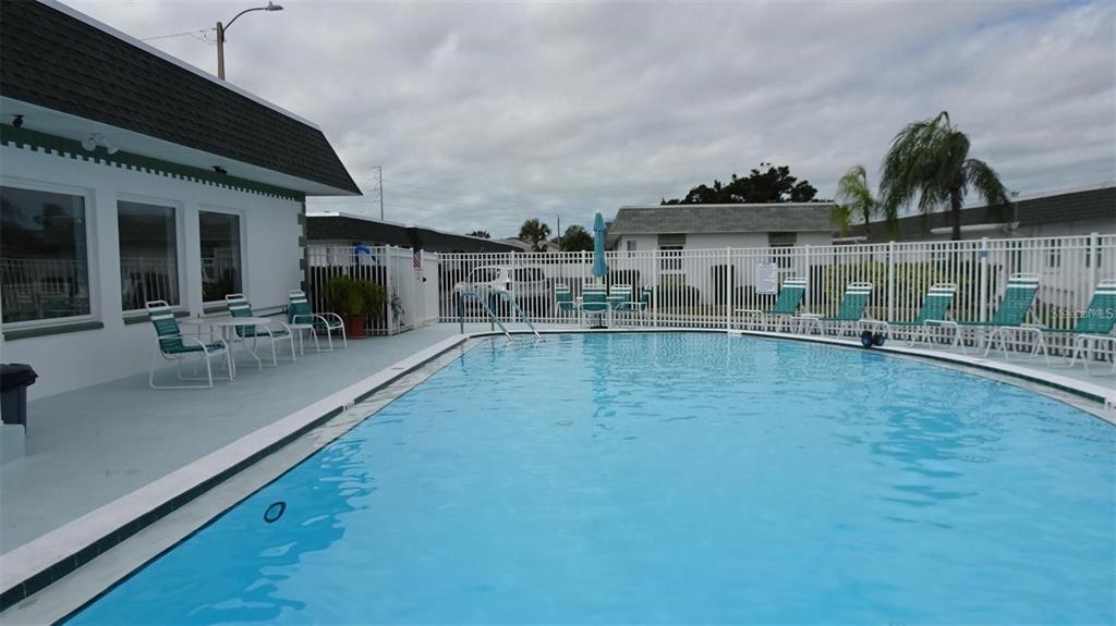 A swimming pool with lounge chairs sits on a patio next to a white building — 7868 40TH AVENUE N UNIT 7868, ST PETERSBURG, FL