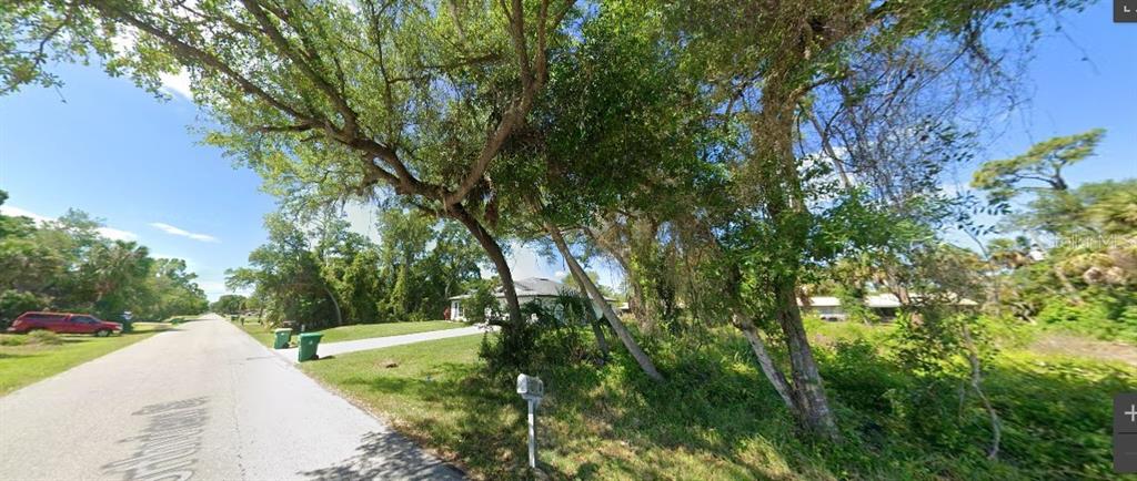 A paved street runs past a grassy lot with mature trees and a distant house — 289 NORTHVIEW STREET, PORT CHARLOTTE, FL
