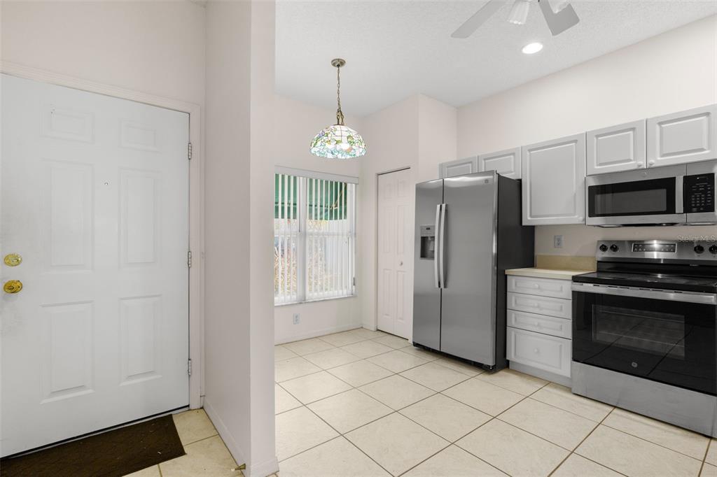 A kitchen with white cabinets, stainless steel appliances, and tile flooring next to a dining area — 6600 100TH WAY N UNIT 24B, ST PETERSBURG, FL
