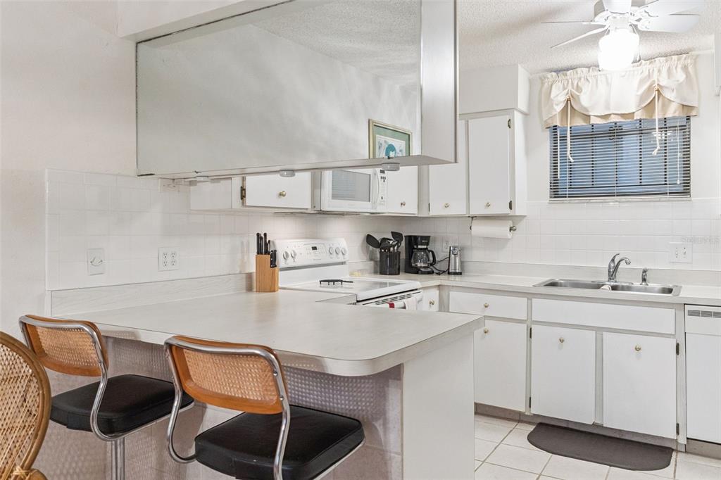 A kitchen features white cabinets, a breakfast bar with stools, and a tiled backsplash — 325 WILDER BOULEVARD UNIT 103, DAYTONA BEACH, FL