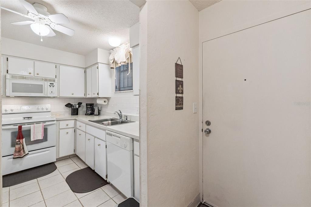 A white kitchen features tile flooring, white cabinets, and a white door on the right — 325 WILDER BOULEVARD UNIT 103, DAYTONA BEACH, FL