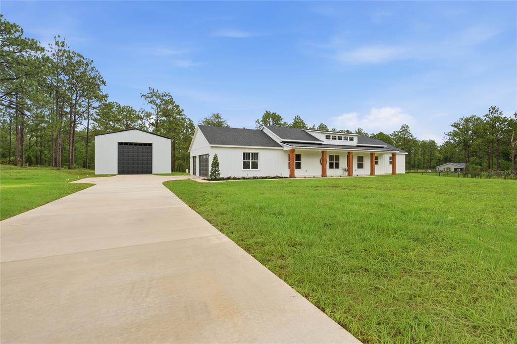 An aerial view of a modern white farmhouse with a black roof and wooden columns — 8730 NW 17TH CIRCLE, OCALA, FL