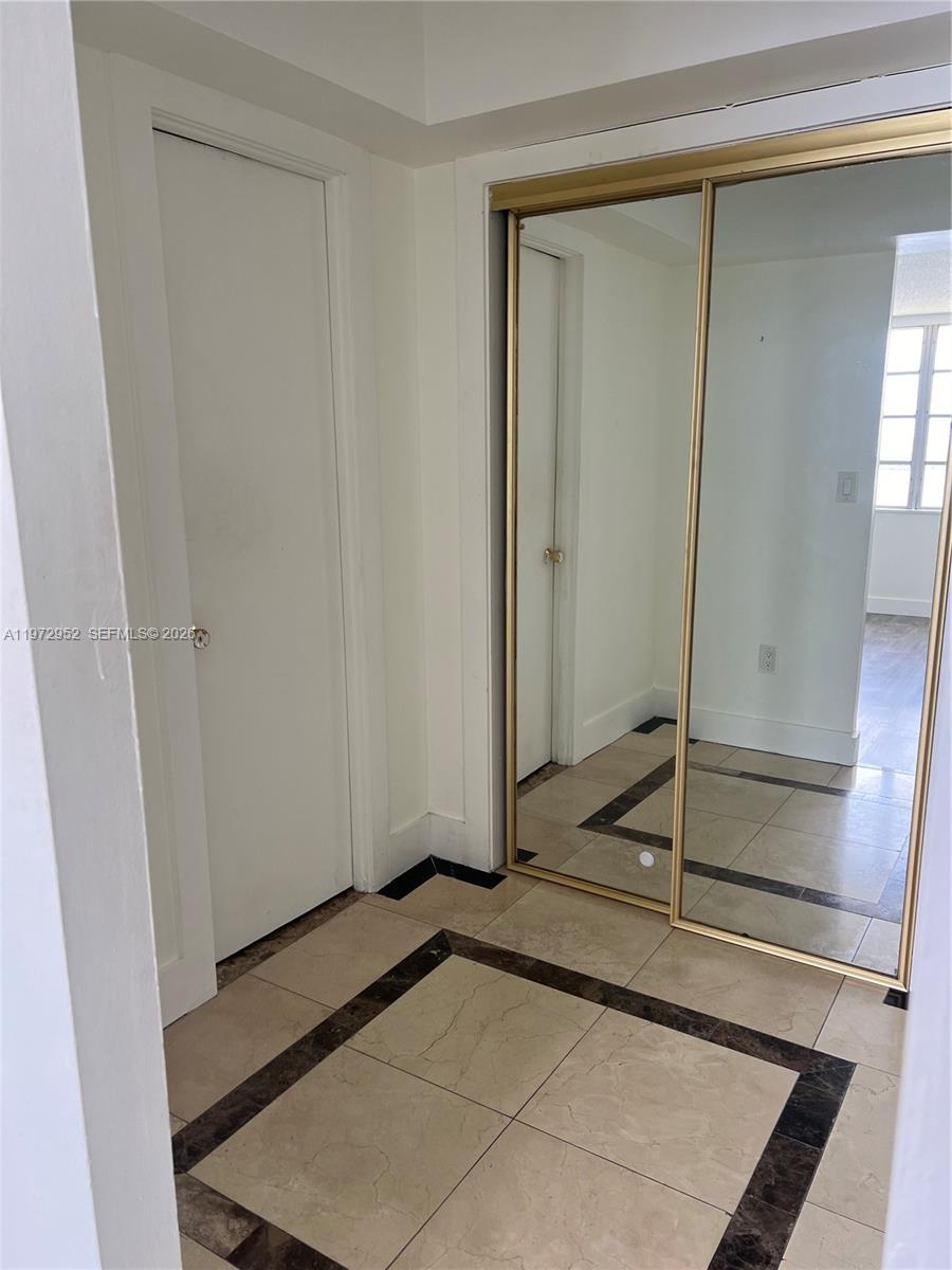 A hallway features beige tiled flooring with dark accents, a white door, and mirrored closets — 18601 NE 14th Ave # 411, Miami FL 33179, MIAMI, FL