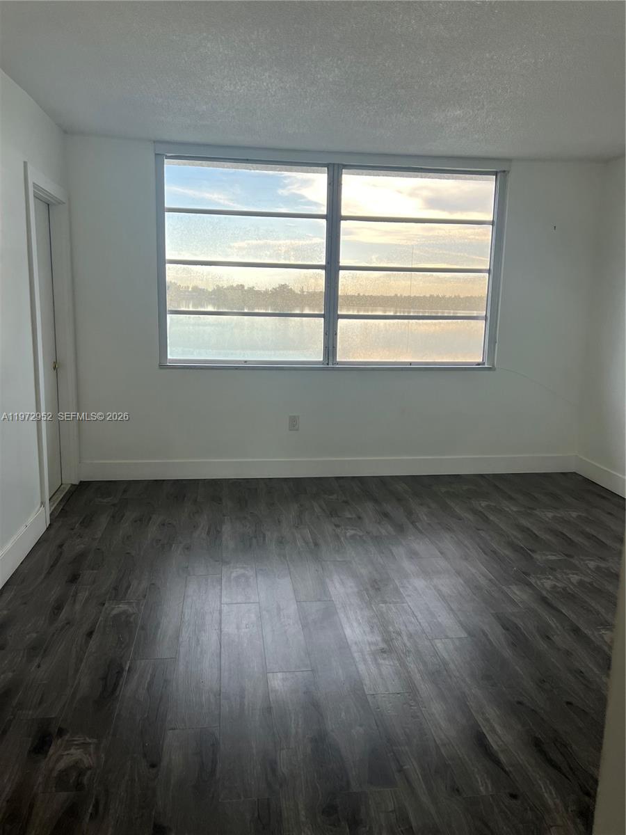 An empty room features dark wood-look flooring, white walls, and a large window overlooking water — 18601 NE 14th Ave # 411, Miami FL 33179, MIAMI, FL