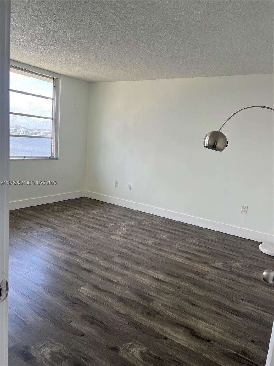 An empty room features dark wood-look flooring, white walls, and a window overlooking water — 18601 NE 14th Ave # 411, Miami FL 33179, MIAMI, FL