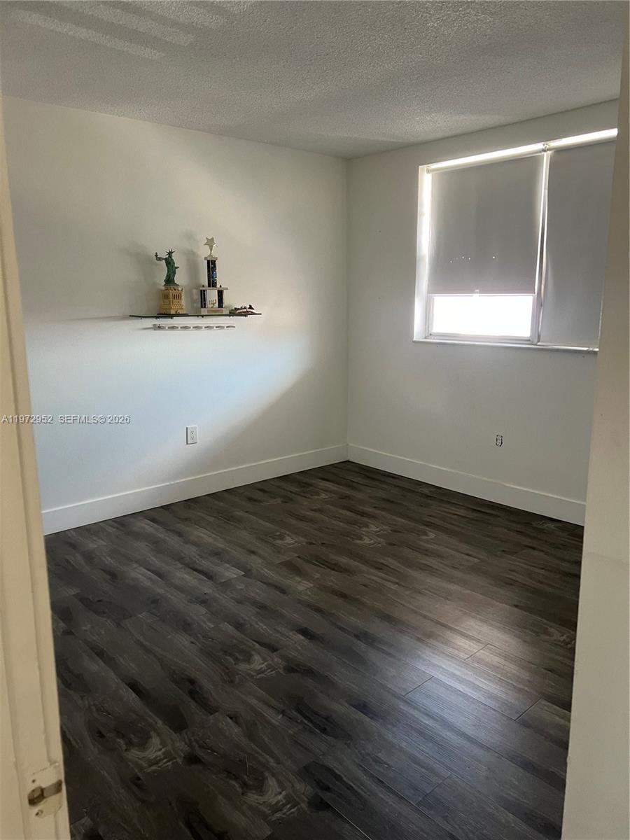 A bedroom features white walls, dark wood-look flooring, a window with a shade, and shelving — 18601 NE 14th Ave # 411, Miami FL 33179, MIAMI, FL