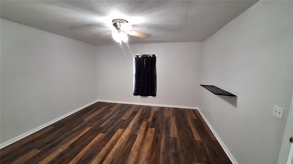An empty bedroom features light gray walls, dark wood-look flooring, a ceiling fan, and a shelf — 80 PECAN PASS, OCALA, FL