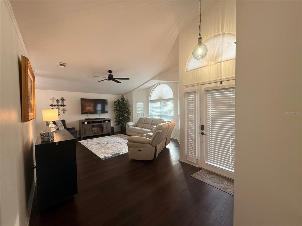 A living room features dark wood floors, vaulted ceilings, a ceiling fan, and white furniture — 6060 CONDOR DRIVE, LAKELAND, FL