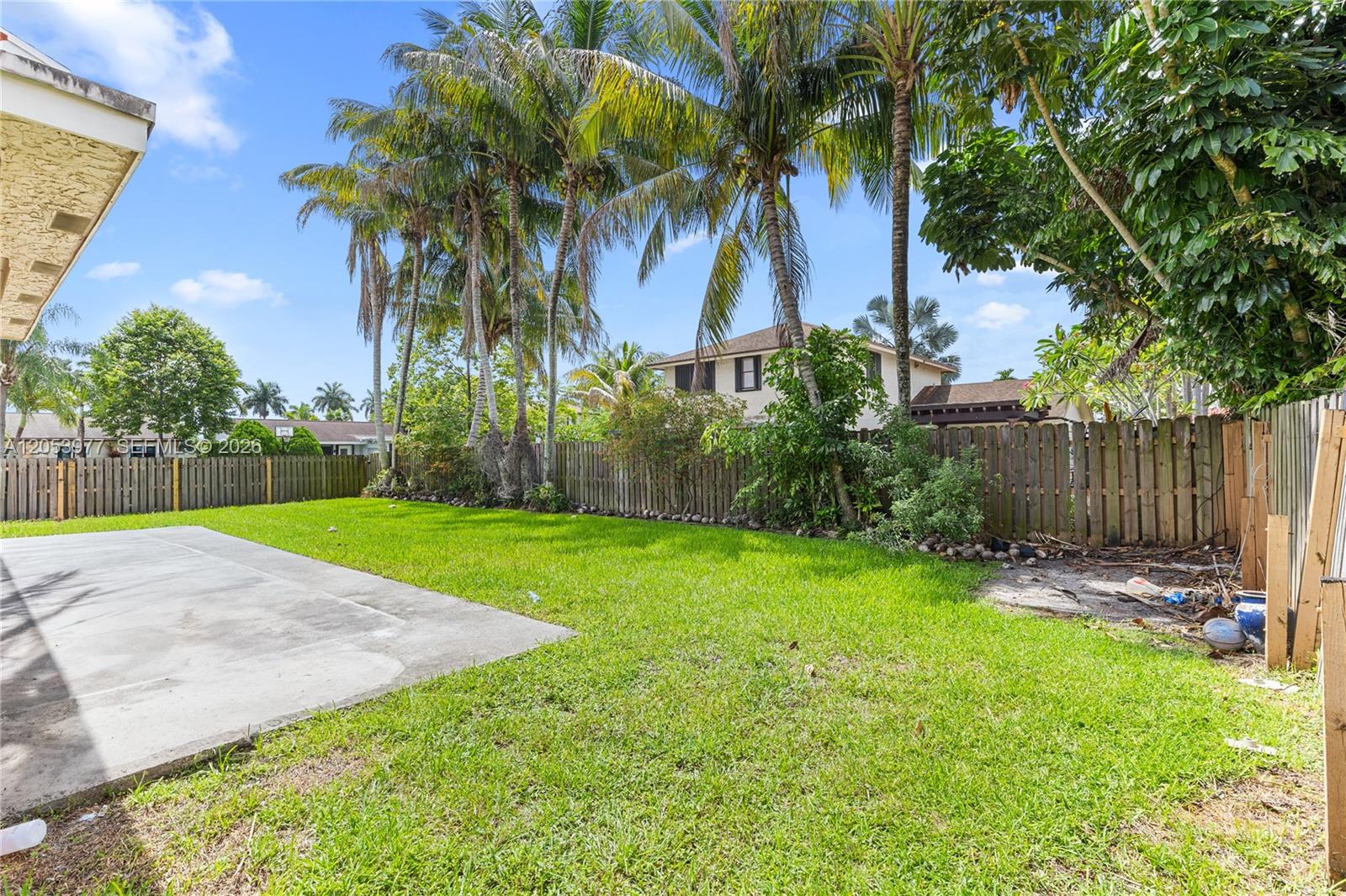 A backyard features a concrete patio, a grassy lawn, palm trees, and a wooden fence — 11610 NW 43rd St, Sunrise FL 33323, SUNRISE, FL