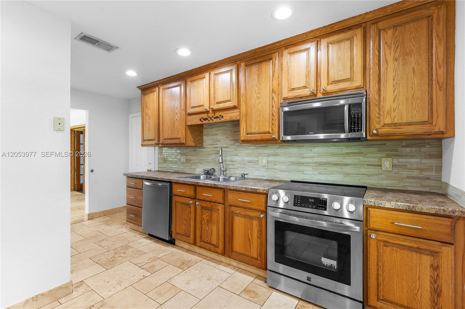 A kitchen features wood cabinets, stainless steel appliances, a tiled backsplash, and stone-look flooring — 11610 NW 43rd St, Sunrise FL 33323, SUNRISE, FL