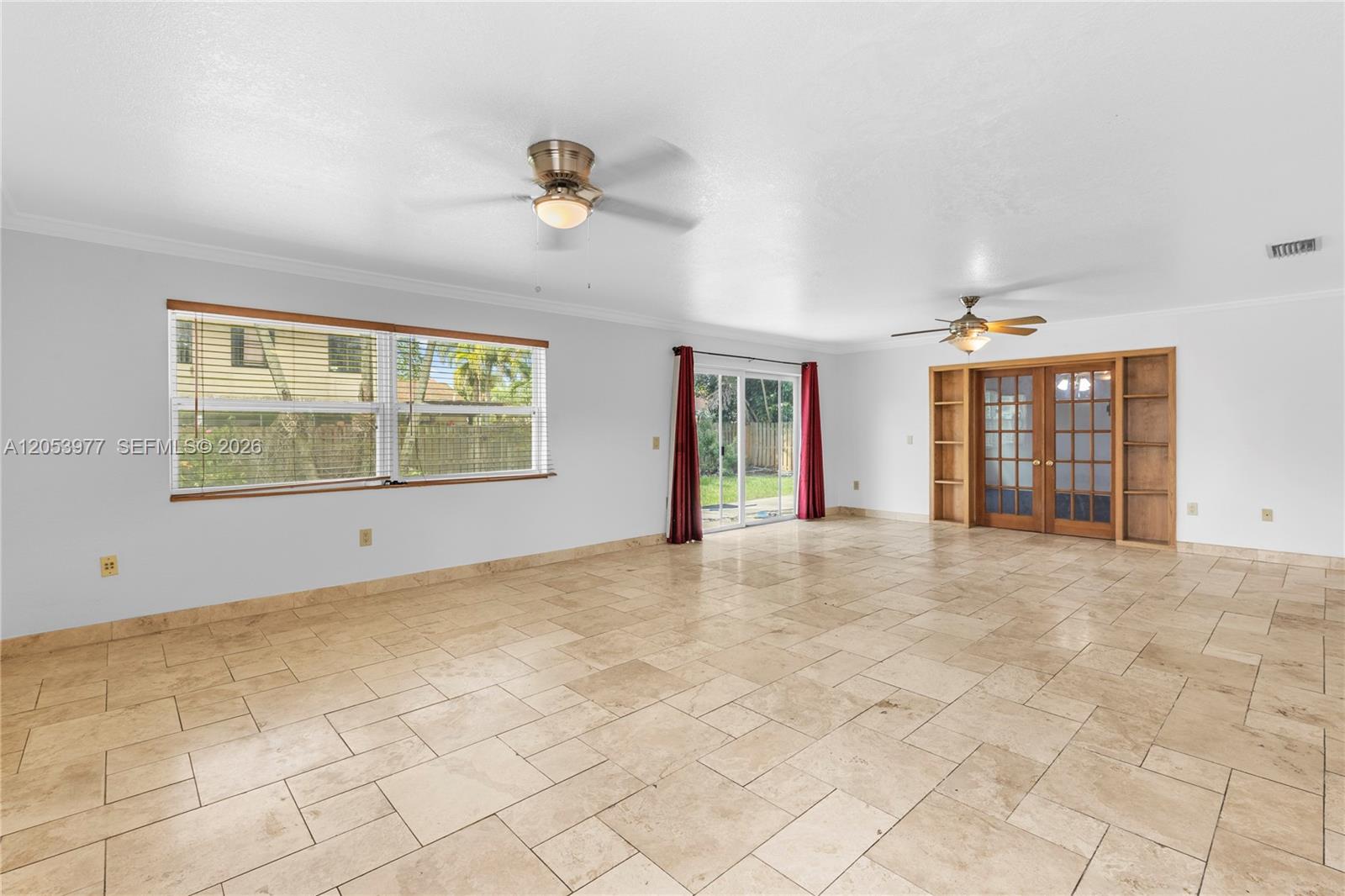 A spacious living room features light-colored tile flooring, two ceiling fans, and wooden French doors — 11610 NW 43rd St, Sunrise FL 33323, SUNRISE, FL