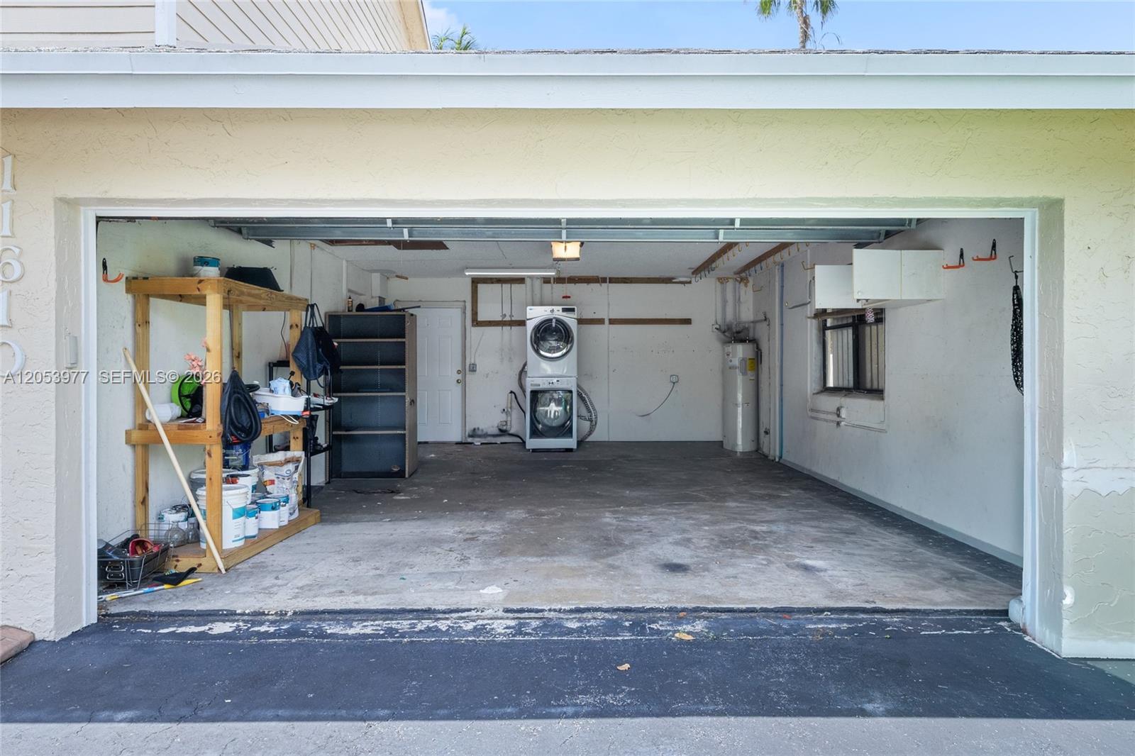 An open garage features a concrete floor, a stacked washer and dryer, and storage shelving — 11610 NW 43rd St, Sunrise FL 33323, SUNRISE, FL