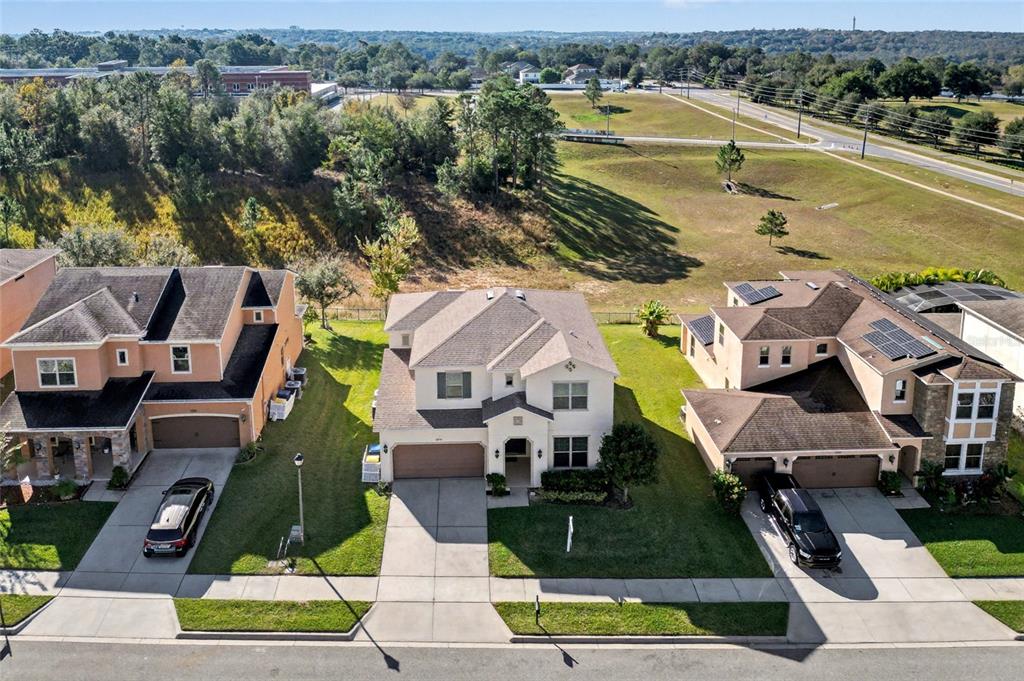 An aerial view shows three suburban houses with driveways and lawns bordering a grassy field — 1244 GATEWOOD AVENUE, MINNEOLA, FL