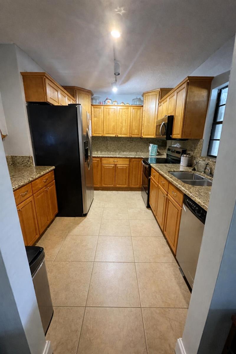 A galley kitchen features honey-oak cabinets, granite countertops, tile flooring, and black appliances — 4052 N Pine Island Road # 1c, Sunrise FL 33351, SUNRISE, FL