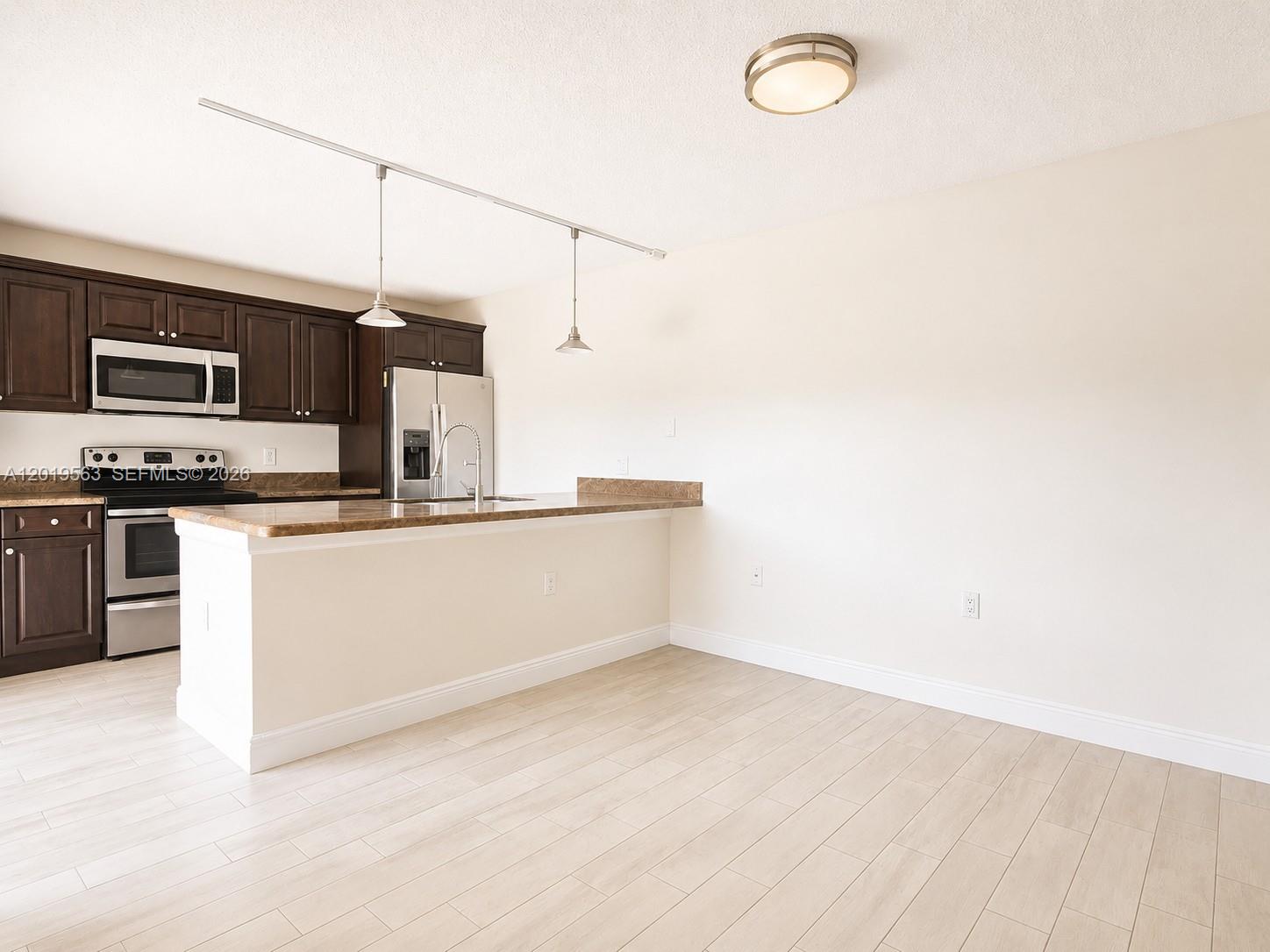 A kitchen features dark wood cabinets, stainless steel appliances, and a breakfast bar island — 824 Blue Ridge Cir, West Palm Beach FL 33409, WEST PALM BEACH, FL