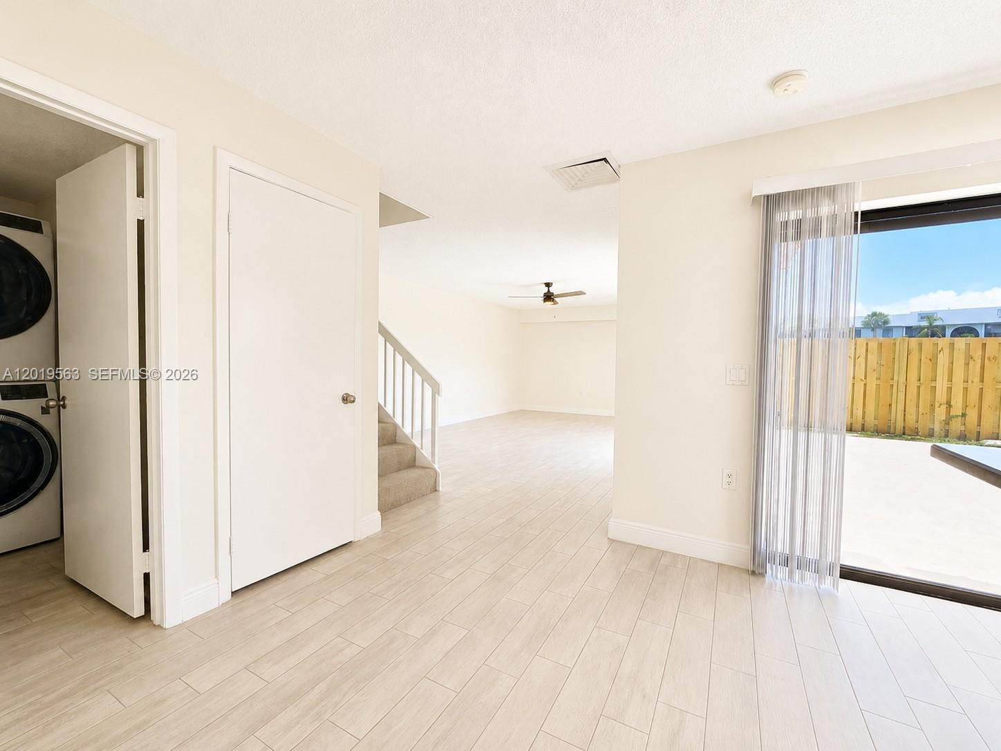 A room with light-colored tile flooring features a laundry closet, staircase, and sliding glass doors — 824 Blue Ridge Cir, West Palm Beach FL 33409, WEST PALM BEACH, FL