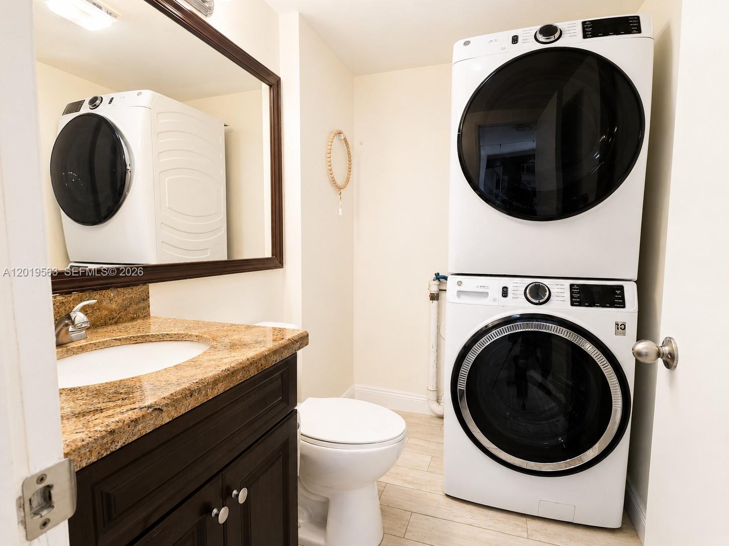 A bathroom features a vanity with a granite countertop, a toilet, and a stacked washer-dryer — 824 Blue Ridge Cir, West Palm Beach FL 33409, WEST PALM BEACH, FL