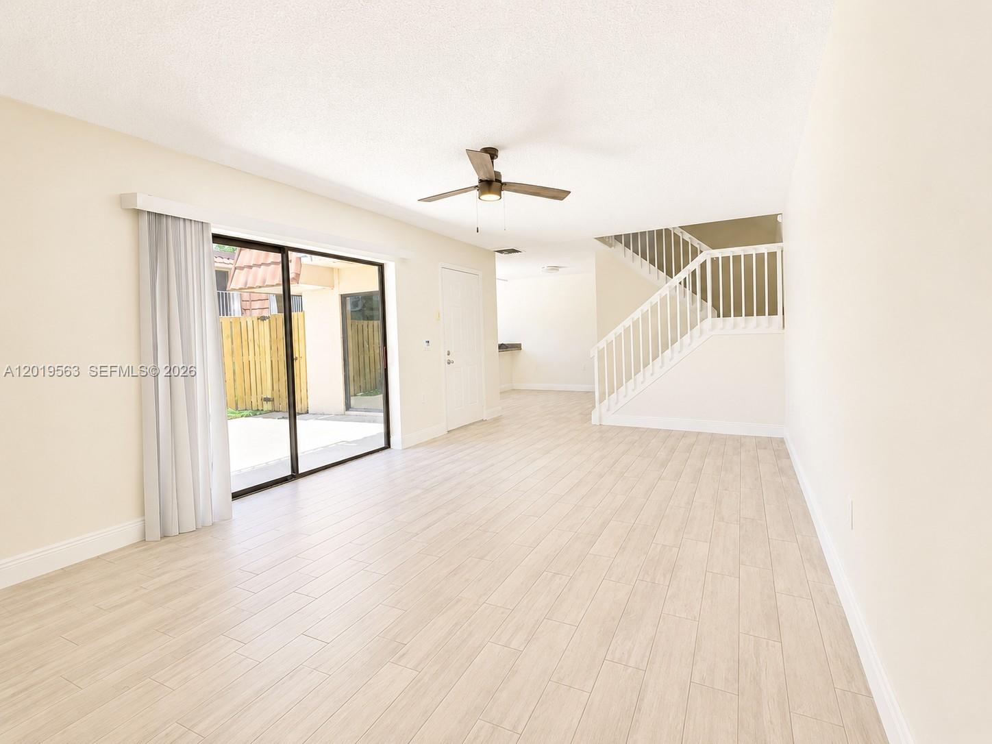 An empty living room features light wood-look flooring, a ceiling fan, and a staircase — 824 Blue Ridge Cir, West Palm Beach FL 33409, WEST PALM BEACH, FL