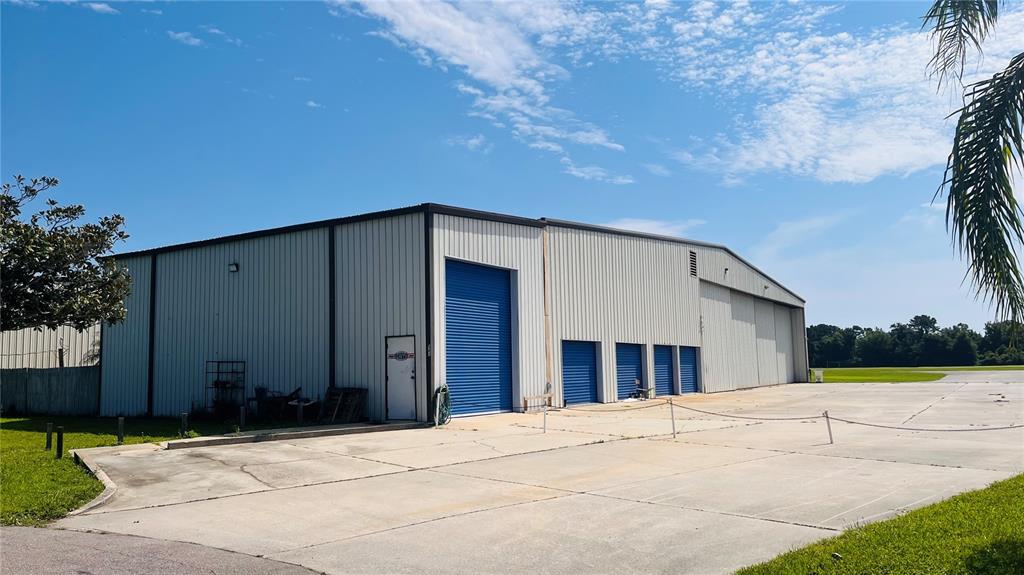 A large metal warehouse building features multiple blue roll-up doors and a concrete parking area — 541 SKYWAY DRIVE, EDGEWATER, FL