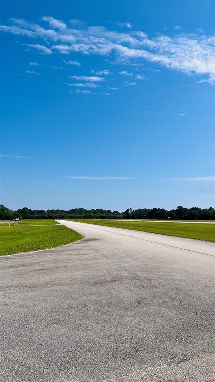 A paved road stretches through a grassy field toward a distant line of trees — 541 SKYWAY DRIVE, EDGEWATER, FL