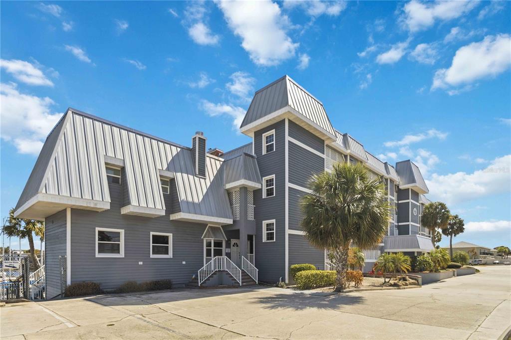 A multi-story gray building with a metal roof stands next to a paved parking lot — 905 N HARBOR CITY BOULEVARD UNIT 204, MELBOURNE, FL