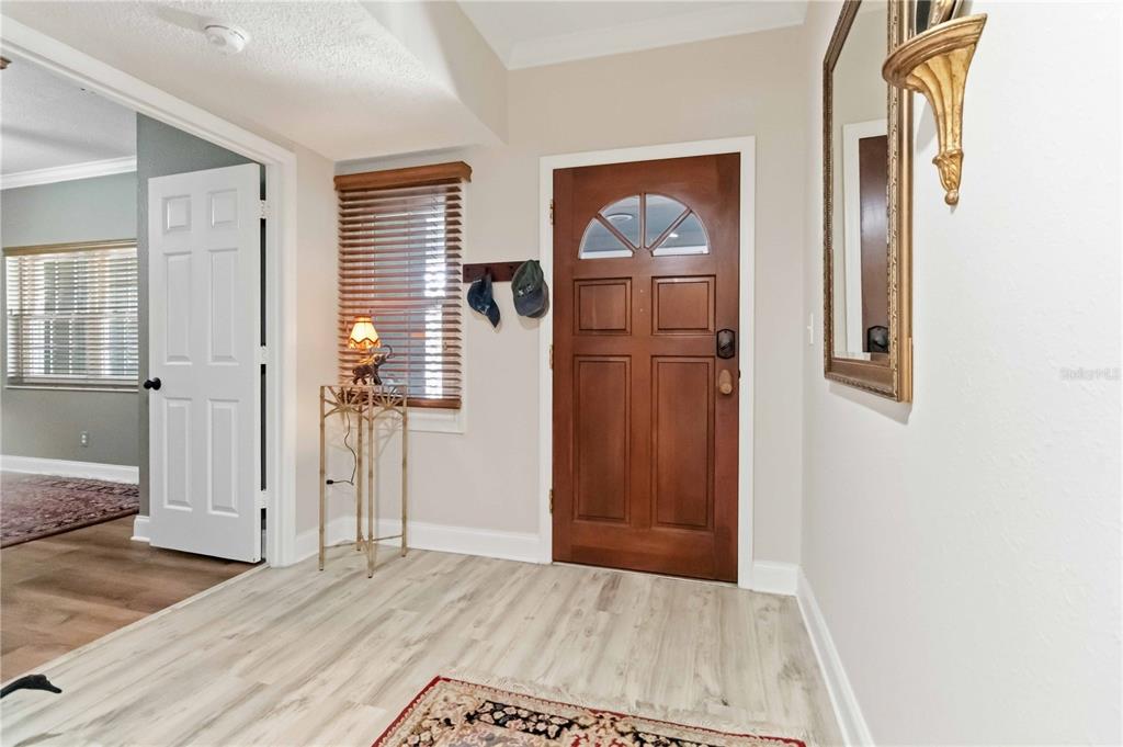 An entryway features light wood-look flooring, a wooden front door, and a wall-mounted mirror — 905 N HARBOR CITY BOULEVARD UNIT 204, MELBOURNE, FL