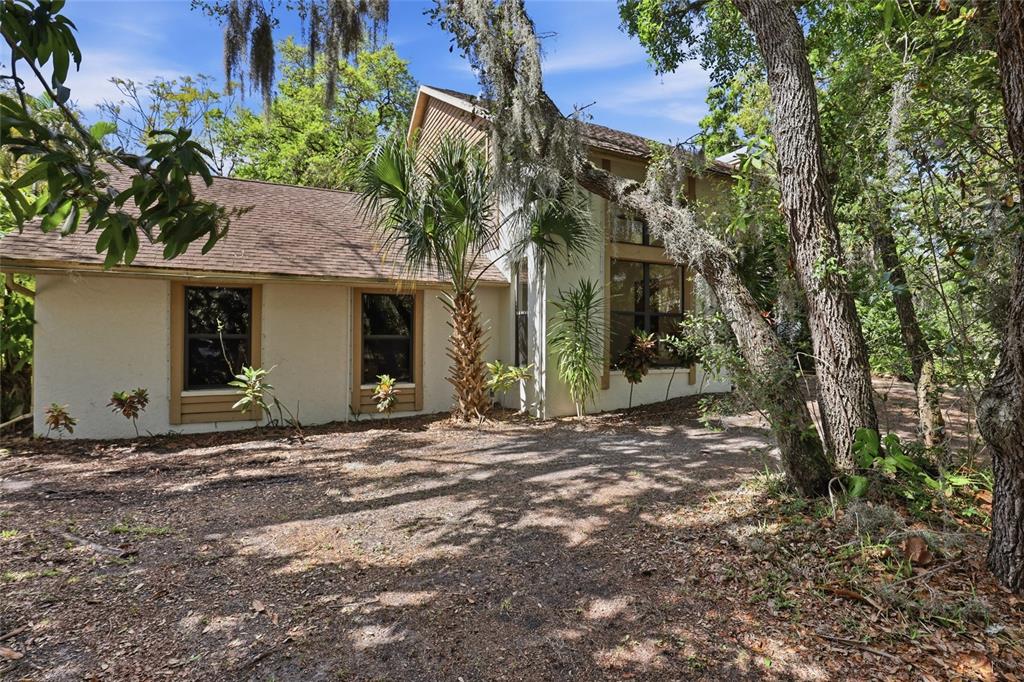 A two-story house with a light-colored exterior and brown roof sits in a wooded area — 7336 CURLEW STREET, SARASOTA, FL
