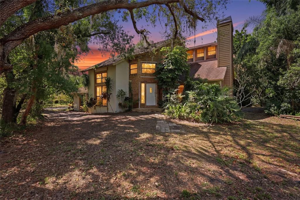 A two-story house with brick and stucco siding sits among trees under a sunset sky — 7336 CURLEW STREET, SARASOTA, FL