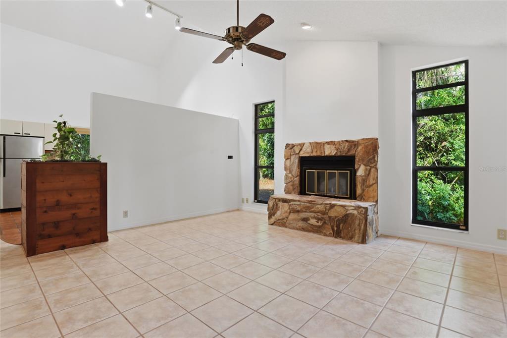 A living room features a stone fireplace, tile flooring, a ceiling fan, and large windows — 7336 CURLEW STREET, SARASOTA, FL