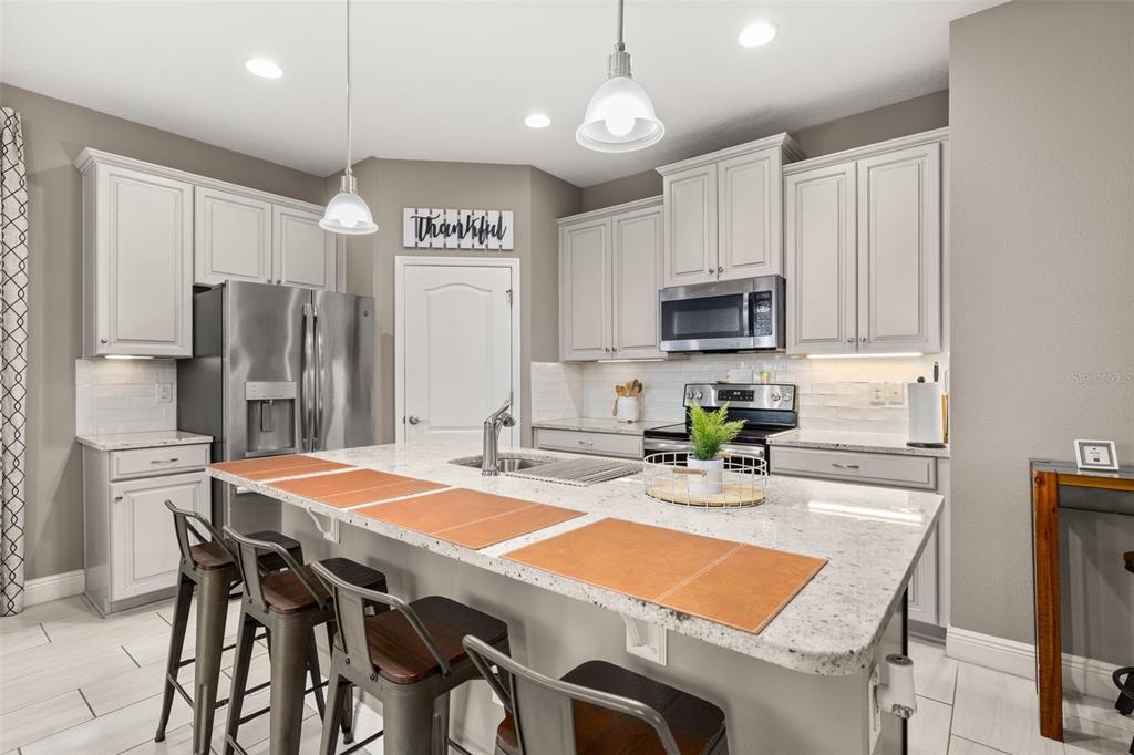 A kitchen features light gray cabinets, granite countertops, a central island, and stainless steel appliances — 17023 GOLDCREST LOOP, CLERMONT, FL