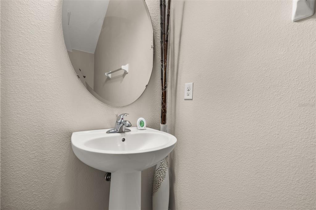 A pedestal sink with a round mirror and decorative sticks stands against a beige wall — 17023 GOLDCREST LOOP, CLERMONT, FL