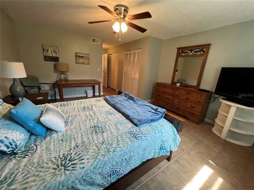 A bedroom features a bed with a patterned quilt, a wooden dresser, and tile flooring — 2100 OCEAN SHORE BOULEVARD UNIT 1150, ORMOND BEACH, FL