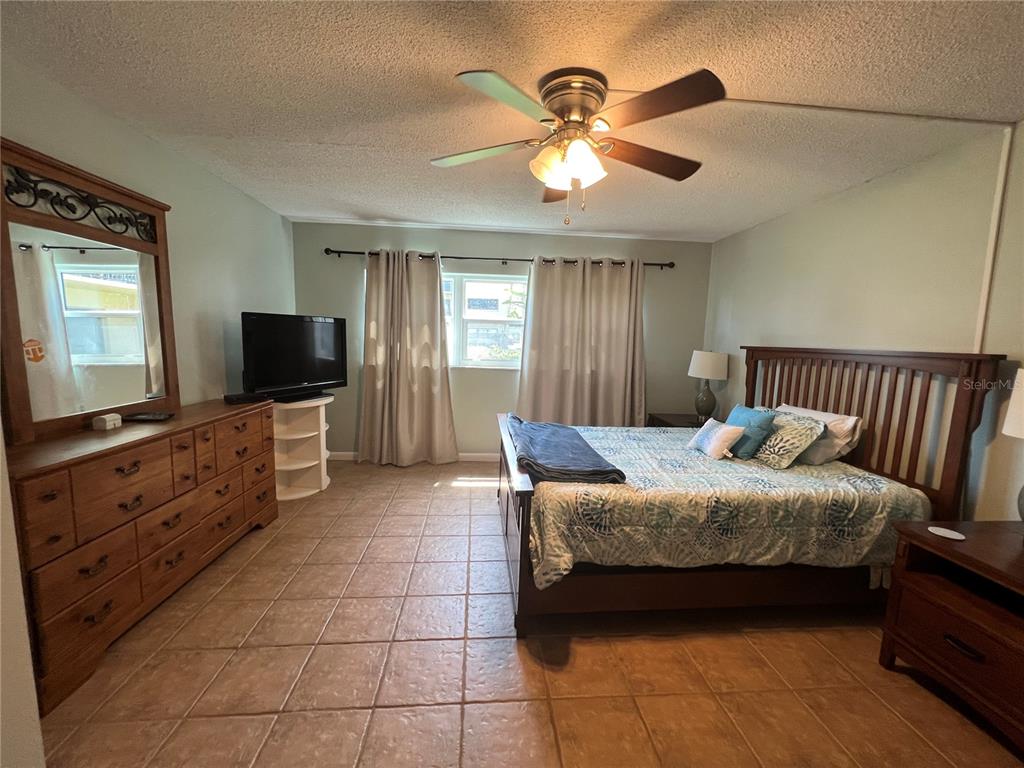 A bedroom features a wooden bed frame, a large dresser with a mirror, and tile flooring — 2100 OCEAN SHORE BOULEVARD UNIT 1150, ORMOND BEACH, FL