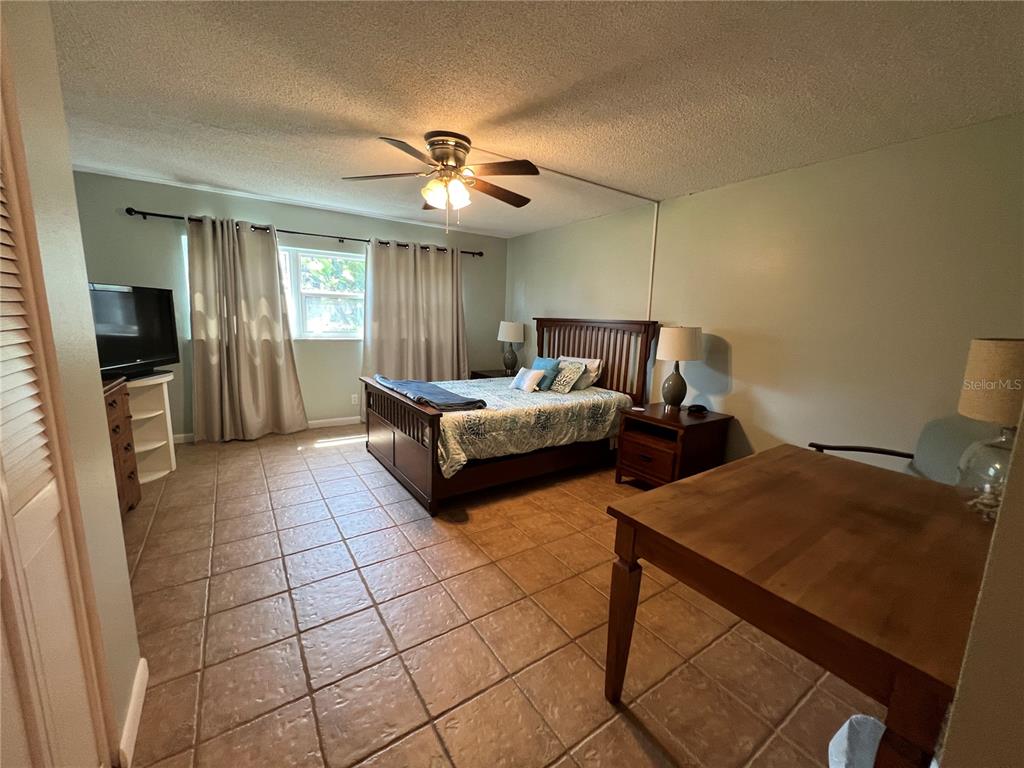 A bedroom features tile flooring, a wooden bed frame, a ceiling fan, and a desk — 2100 OCEAN SHORE BOULEVARD UNIT 1150, ORMOND BEACH, FL