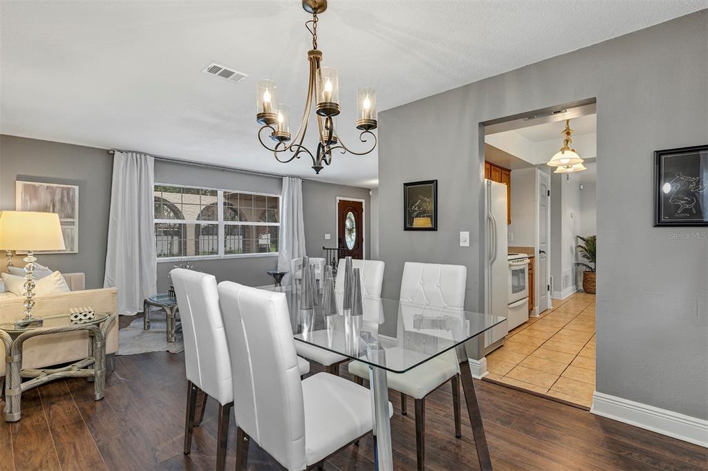 A dining room with a glass table, white chairs, and a chandelier, adjacent to a kitchen — 521 AMERICAN HERITAGE PARKWAY, ORLANDO, FL