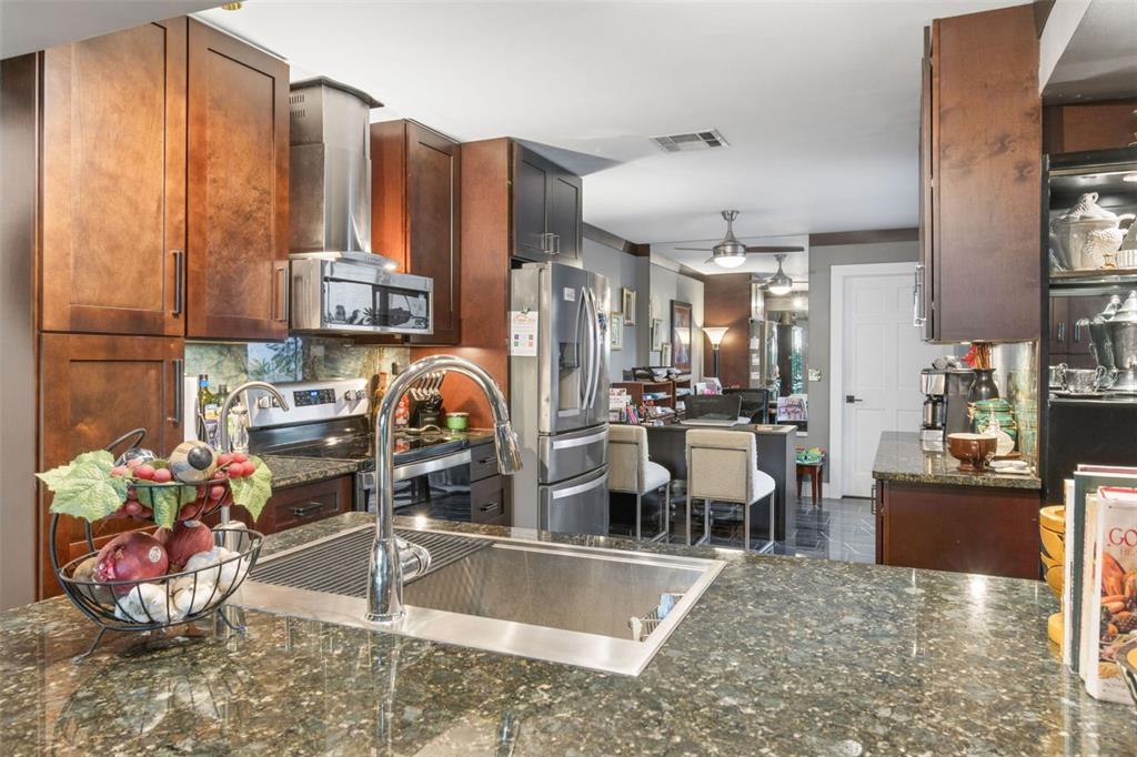 A kitchen with dark wood cabinets, granite countertops, stainless steel appliances, and a central island — 7913 BAYSIDE VIEW DRIVE, ORLANDO, FL