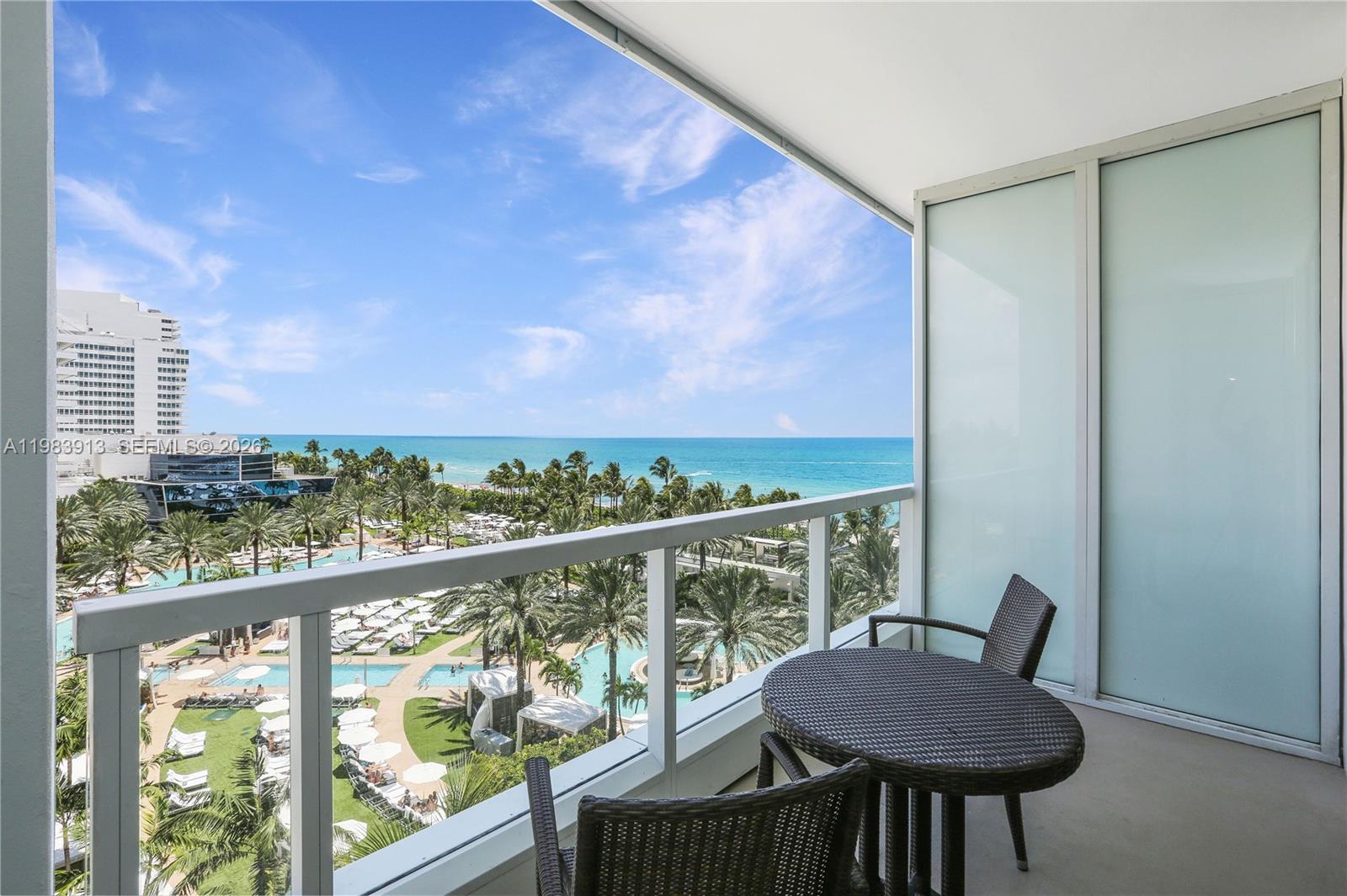 A balcony with a table and chairs overlooks a resort pool and the ocean — 4391 Collins Ave # 605, Miami Beach FL 33140, MIAMI BEACH, FL