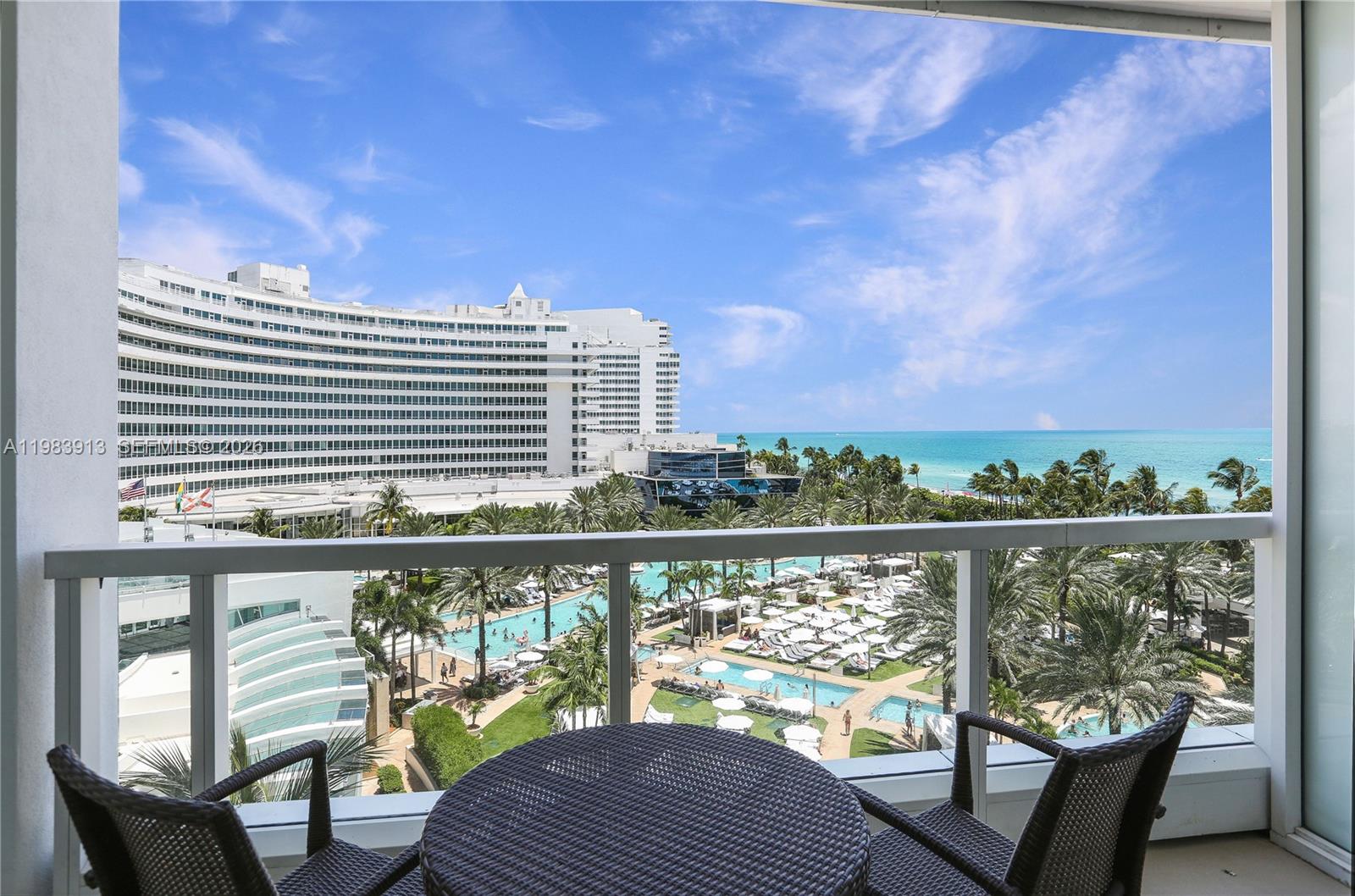 A balcony with outdoor furniture overlooks a large resort pool and the ocean — 4391 Collins Ave # 605, Miami Beach FL 33140, MIAMI BEACH, FL
