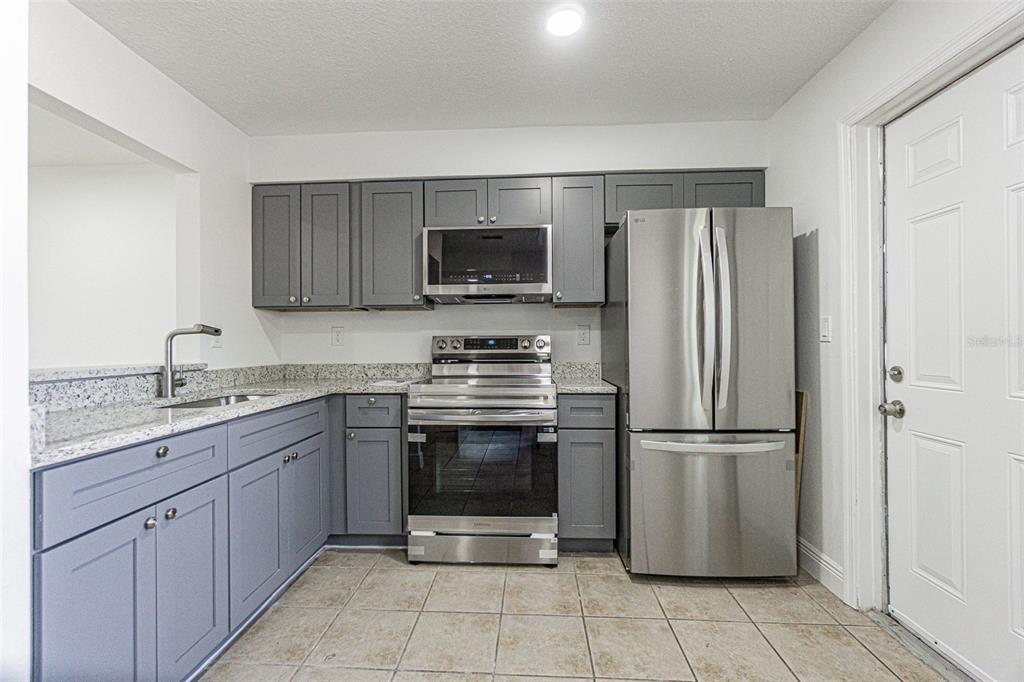 A kitchen features gray cabinets, stainless steel appliances, granite countertops, and tile flooring — 556 CLEARWATER LARGO ROAD N UNIT D, LARGO, FL