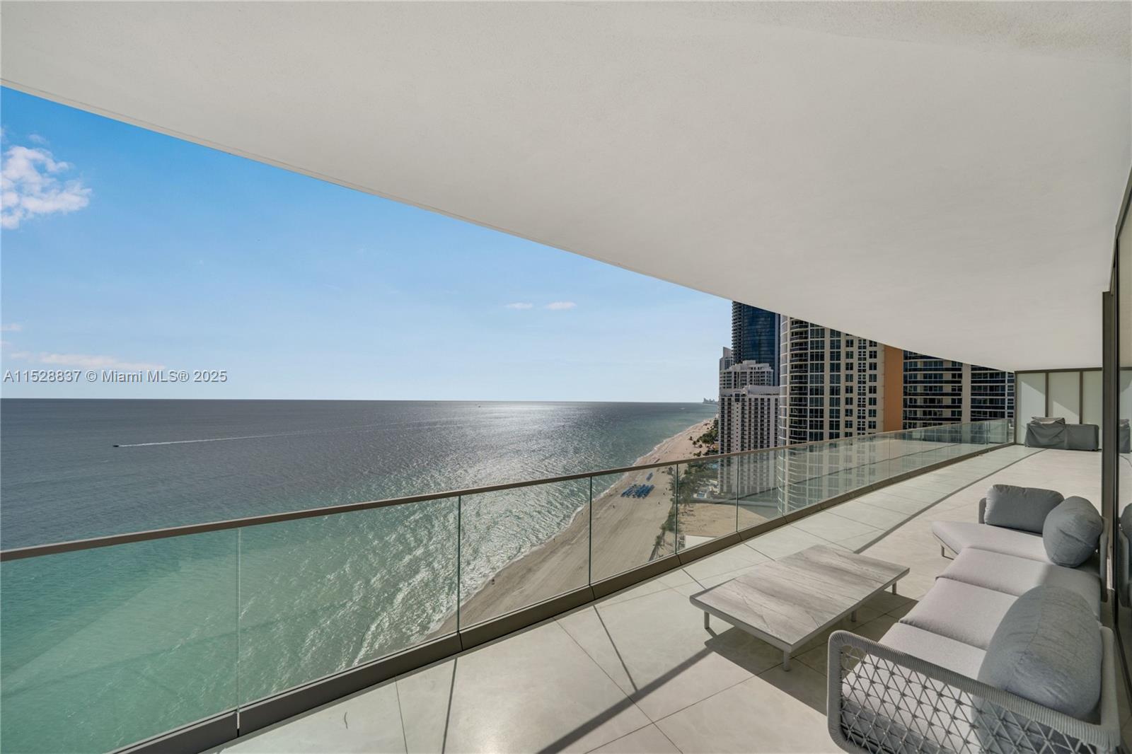 A spacious balcony features a glass railing, outdoor seating, and a panoramic ocean view — 18975 Collins Ave # 2000, Sunny Isles Beach FL 33160, SUNNY ISLES BEACH, FL