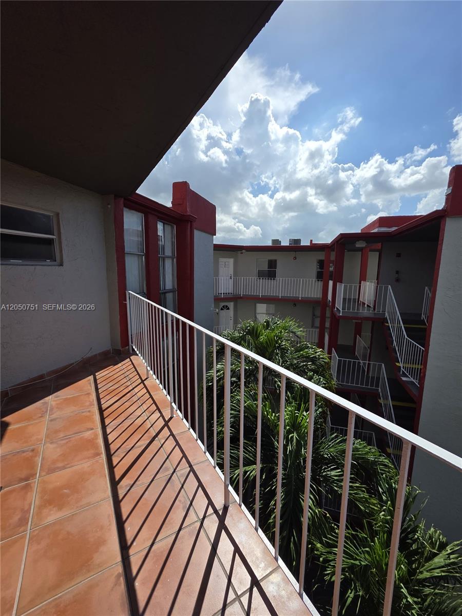 A view from a tiled balcony overlooking a courtyard with palm trees and exterior walkways — 1750 W 46th St # 520, Hialeah FL 33012, HIALEAH, FL